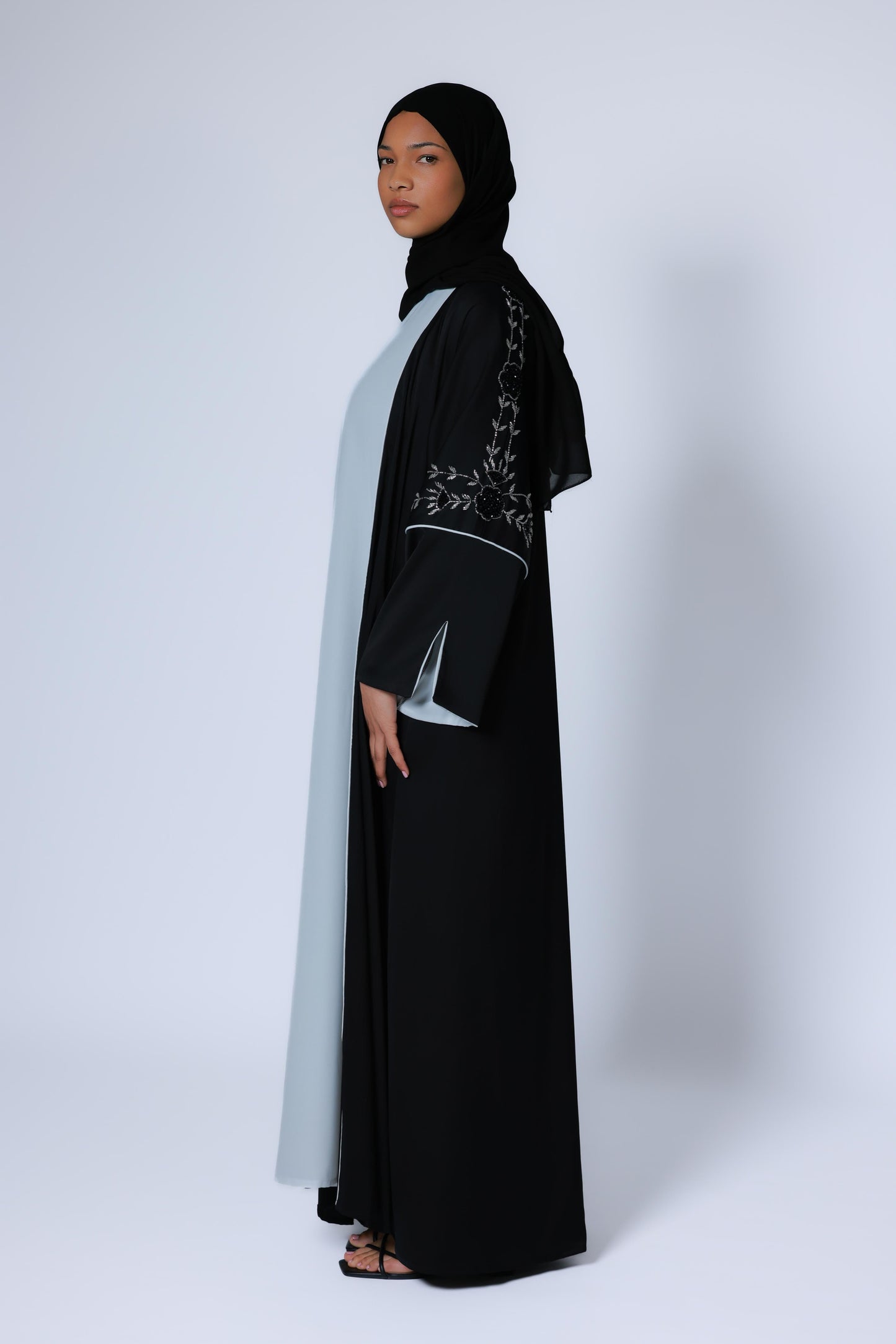 Zwarte open abaya met subtiele zilveren details op de mouwen en wjtte onderjurk, studiofoto