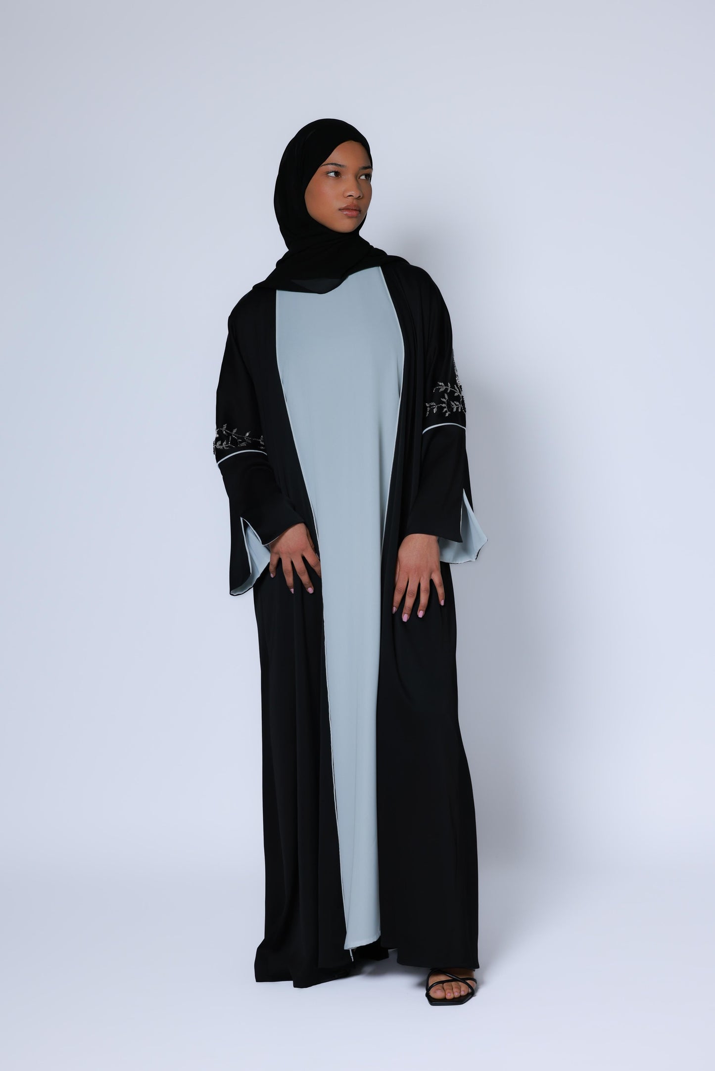 Elegante zwarte abaya met wijde mouwen en zilveren borduursel, gecombineerd met een witte binnenjurk