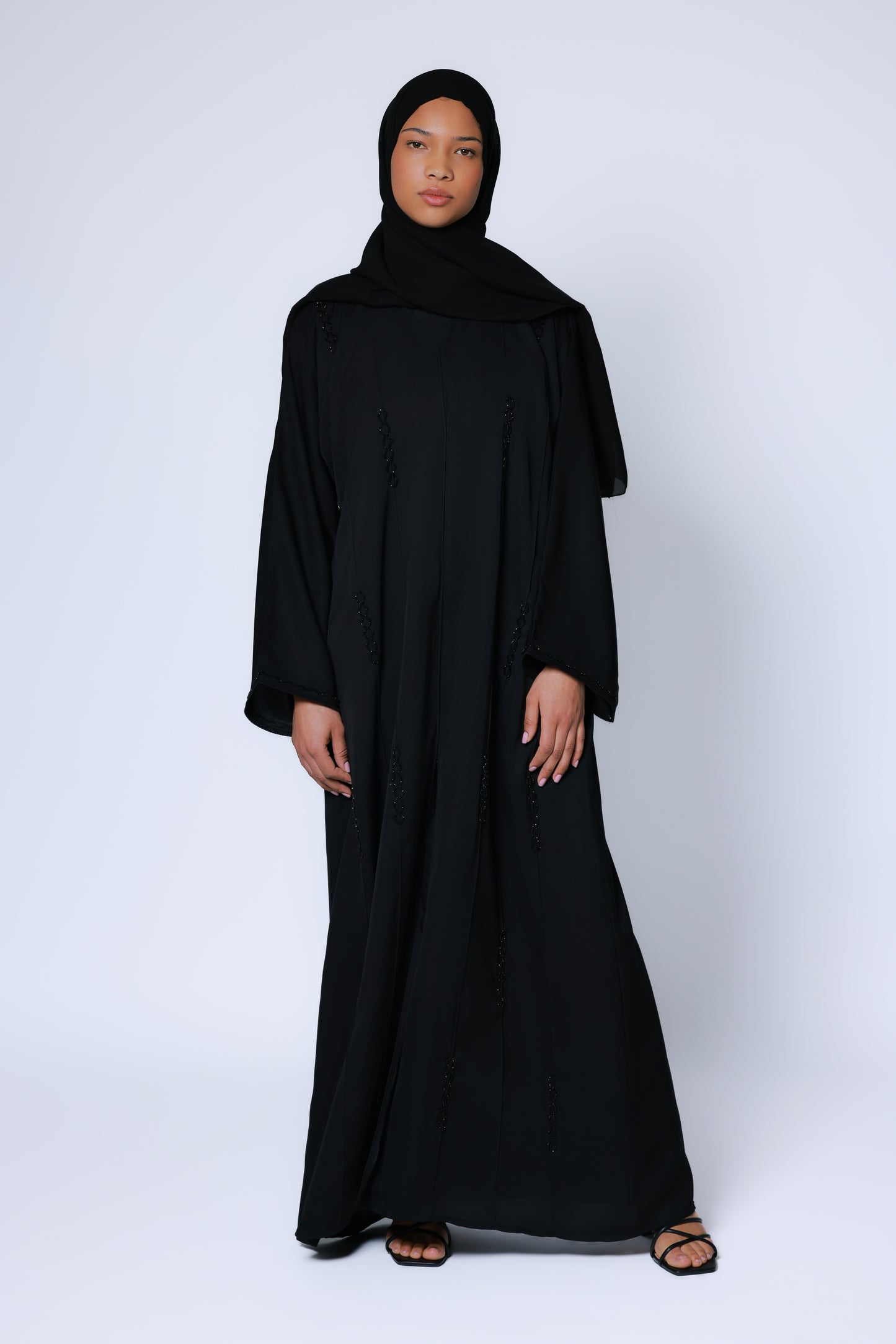 Volledige vooraanzicht van een elegante zwarte abaya met fijne zwarte kraaldetails