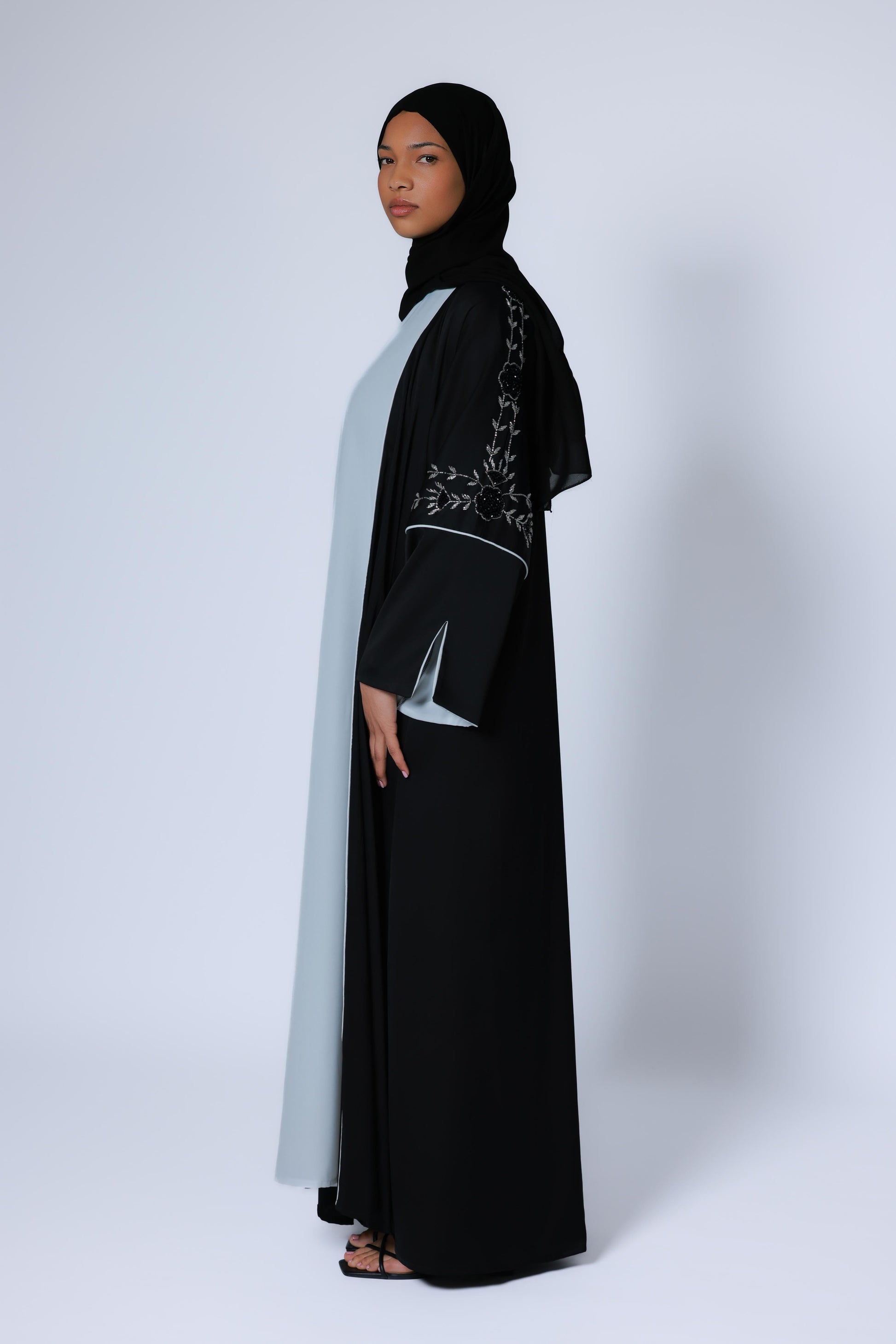 Zwarte open abaya met subtiele zilveren details op de mouwen en wjtte onderjurk, studiofoto