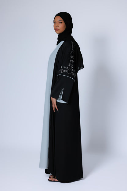 Zwarte open abaya met subtiele zilveren details op de mouwen en wjtte onderjurk, studiofoto