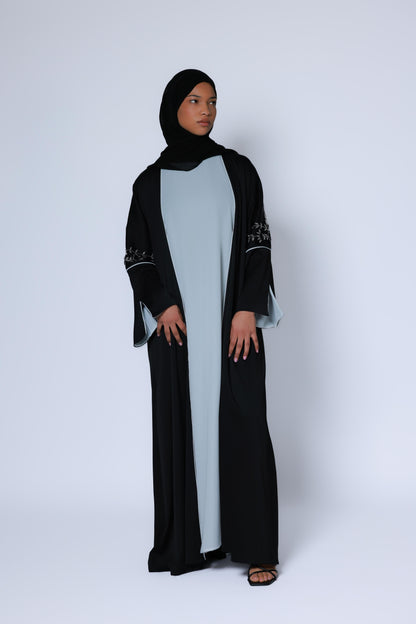 Elegante zwarte abaya met wijde mouwen en zilveren borduursel, gecombineerd met een witte binnenjurk