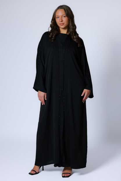 Abaya dames zwart met elegante kimono-snit, gedragen in staande pose met neutrale achtergrond