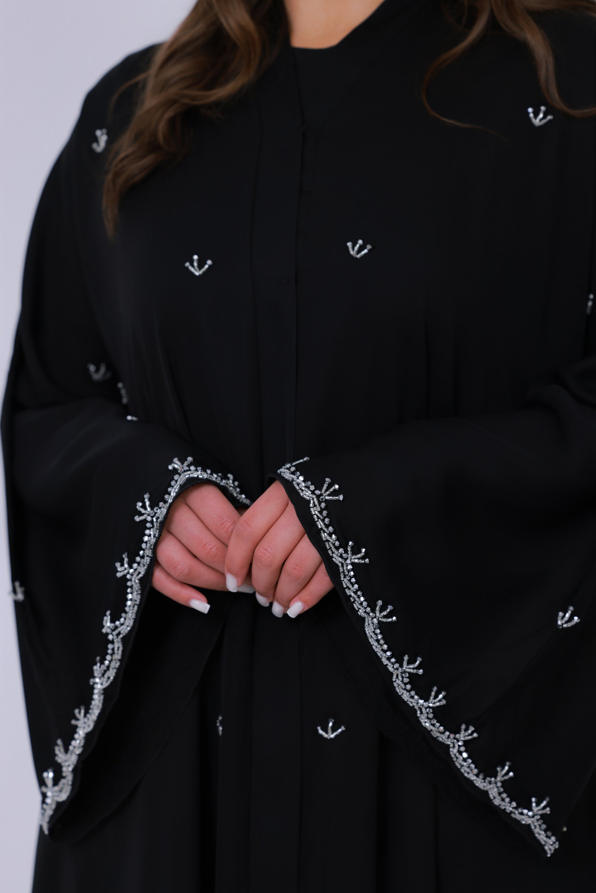 Close-up van zwarte abaya mouwrand met fijn zilverkleurig borduurwerk