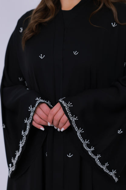 Close-up van zwarte abaya mouwrand met fijn zilverkleurig borduurwerk