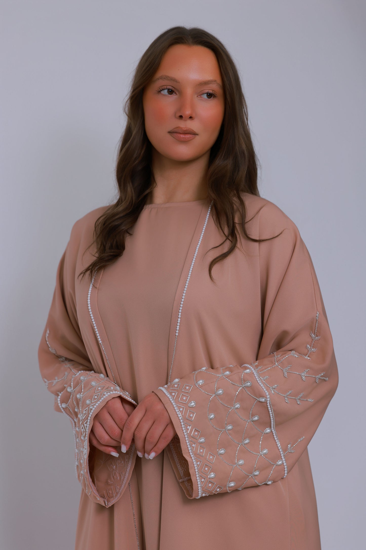 Detail van sand kleurige abaya met parelrand langs de open voorkant
