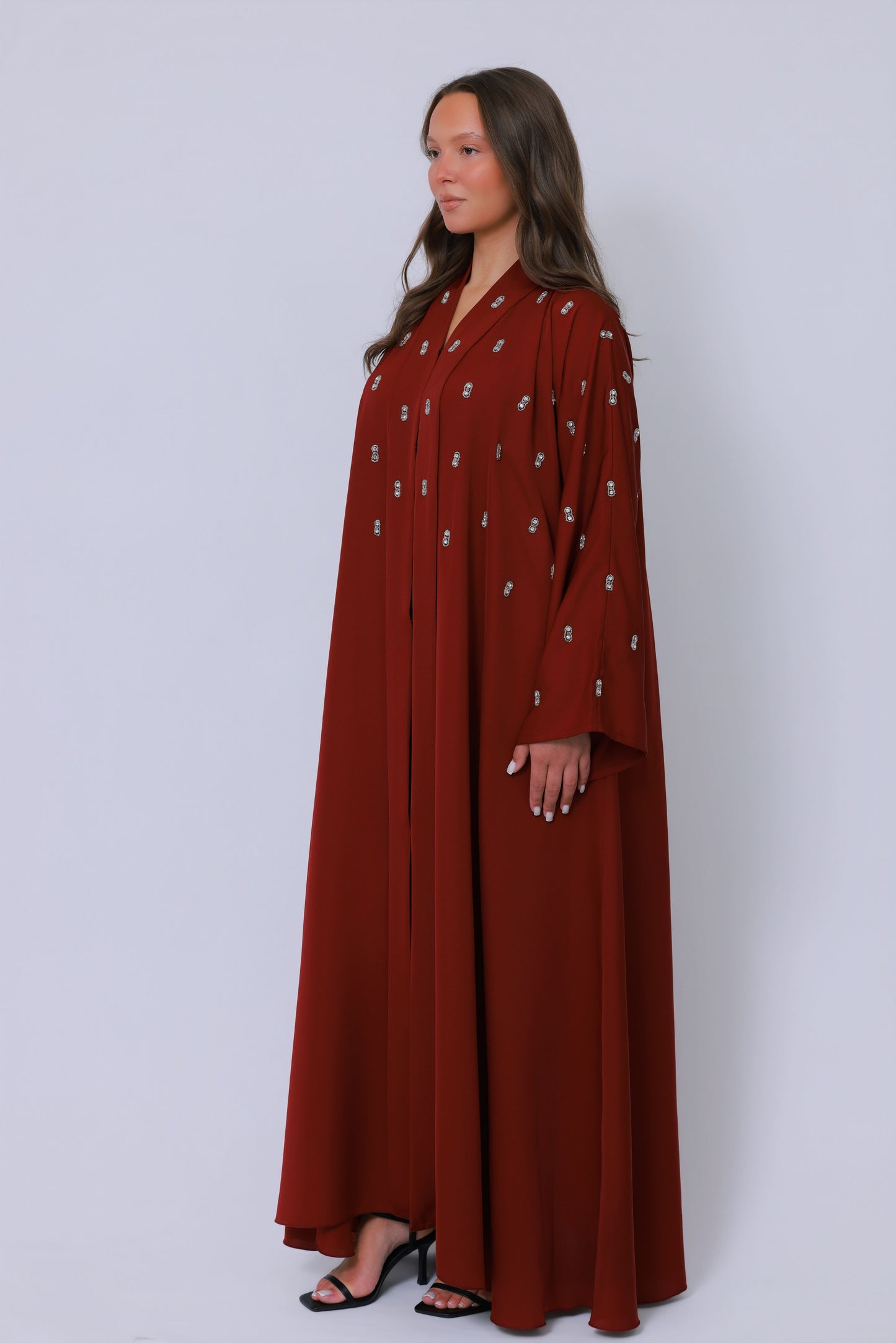 Rode open abaya in schuin perspectief met sierlijk borduurwerk langs de mouwen
